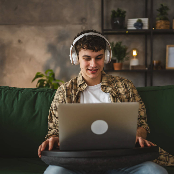 один іонг чоловік білий підліток сидить вдома з навушниками дивитися онлайн фільм відео або серіал на ноутбуці - Фото, зображення
