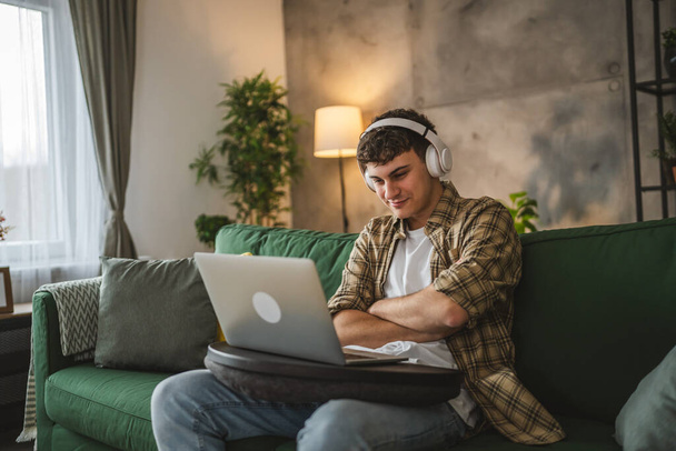een yong man Kaukasische mannelijke tiener zitten thuis met hoofdtelefoon bekijk online film video of serie op laptop - Foto, afbeelding