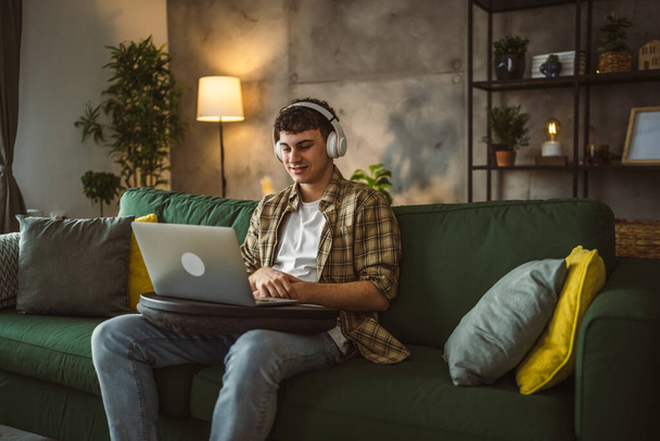 un yong uomo caucasico adolescente maschio sedersi a casa con le cuffie guardare film online video o serie sul computer portatile - Foto, immagini