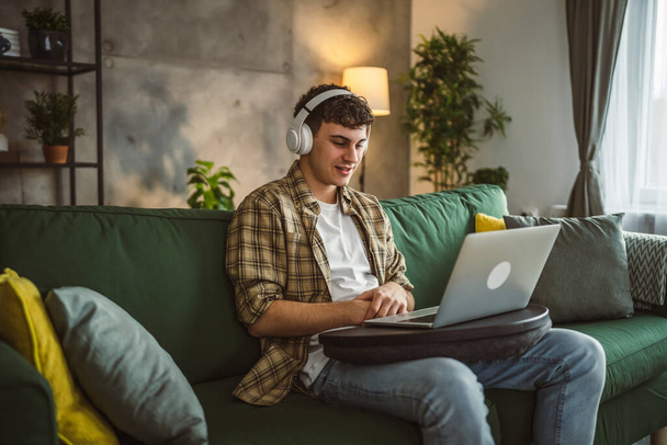 een yong man Kaukasische mannelijke tiener zitten thuis met hoofdtelefoon bekijk online film video of serie op laptop - Foto, afbeelding