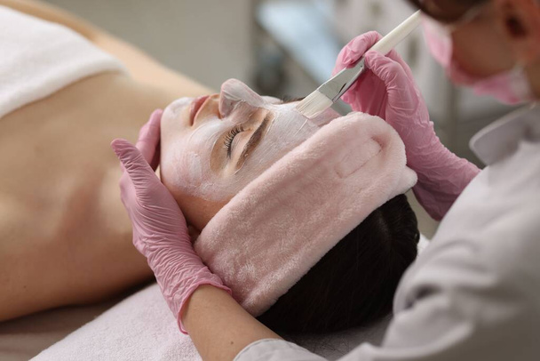 Cosmetoloog aanbrengen van masker op het gezicht van de vrouw, close-up - Foto, afbeelding