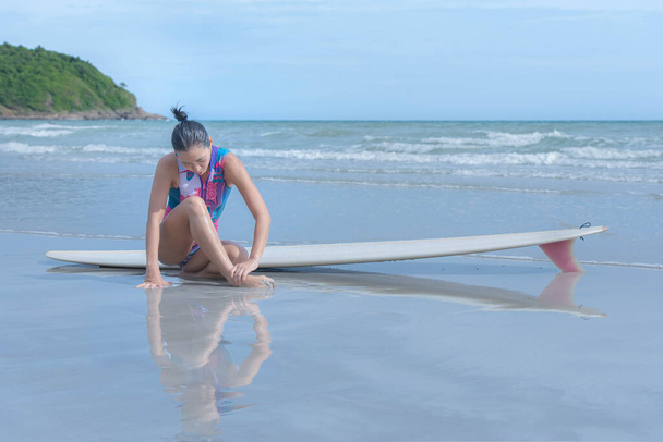 Mujer asiática sentada en la playa, se lesionó el tobillo después de hacer ejercicio surfeando en el mar. con el cuidado de la salud de las personas y el concepto de tablas de surf - Foto, imagen