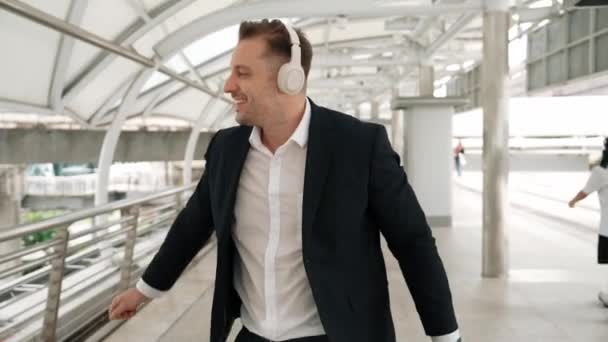 Boldog üzletember táncol, miközben fejhallgatót visel a városban lévő hídnál. Energetikai menedzser vidám és motivációs előadás mozog a zene, hogy megünnepeljük a sikeres projekt, miközben sétálnak. Urbane. - Felvétel, videó