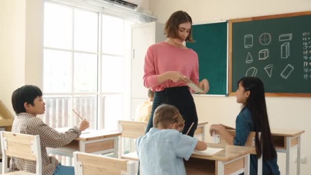 Inteligentny azjatycki uczeń podniósł rękę i pytając nauczyciela o pytanie matematyczne podczas spaceru nauczyciela i sprawdzania pracy domowej w szkole podstawowej. Nauczyciel odpowiada na pytania podnosząc notatnik. Pedagogika. - Materiał filmowy, wideo