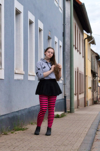 ドイツのローンズフェルド2021年5月16日:ドイツのローンズフェルドの青い建物の前に歩道に立っているピンクと黒のタイツを着たティーンエイジャーの少女. - 写真・画像