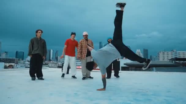 Professionele hipster doen bevriezen pose tijdens het verplaatsen van voetstap naar muziek op het dak met uitzicht op de stad. Break danser voeren straatdans uit omringd door hip-hop dansersgroep. Outdoor sport 2024. hiphop. - Video