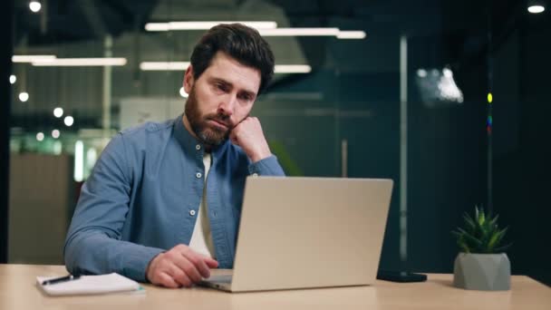 Nieszczęśliwy męski księgowy piszący na przenośnym komputerze i kończący pracę czując się zmęczonym. Śpiący mężczyzna w nieformalnym stroju ziewa i zakrywa usta czekając na koniec nudnego dnia pracy. - Materiał filmowy, wideo