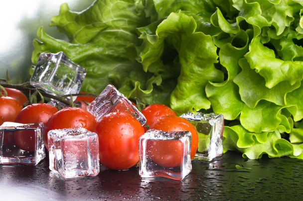 Banch of red cherry tomatos, green salad and ice cubes on black  - Foto, afbeelding