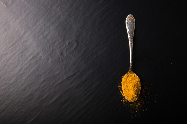 Old metal spoon with spices on a black background - Foto, Bild