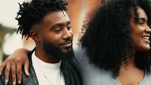 若い幸せなアフリカ系アメリカ人のカップルは笑って一緒に笑い,都市環境の外で笑いながらボーイフレンドの周りに腕を持つ女性 - 写真・画像