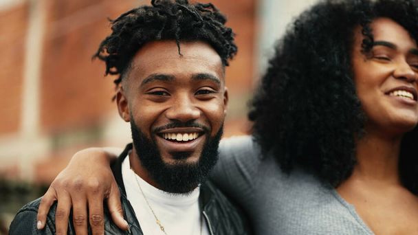 Молодая счастливая афроамериканская пара улыбается и смеется вместе, женщина обнимает своих парней откровенным смехом на улице в городской обстановке - Фото, изображение