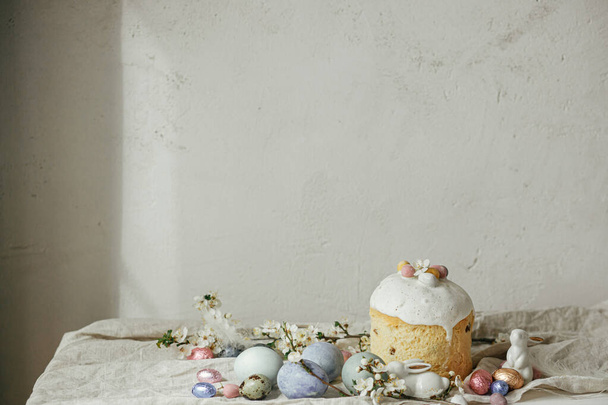 Vrolijk Pasen! Stijlvolle paaseieren, taart, konijntjes, kersenbloesem op rustieke tafel. Moderne natuurlijke geverfde eieren, vakantievoedsel en lentebloemen. Paasland stilleven - Foto, afbeelding