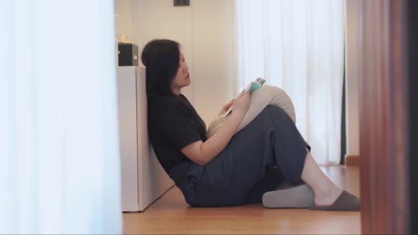 wellness a pohoda koncept s asijskou ženou lehnout a číst knihu v obývacím pokoji - Záběry, video