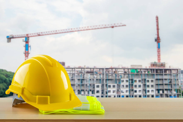 Желтый защитный шлем на деревянном столе с фоном строительной площадки - Фото, изображение