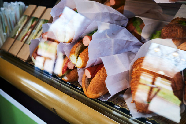 sanduíches, cachorros-quentes e croissants na vitrine refrigerada do restaurante. Refrigerador de contador Deli com comida de retirada - Foto, Imagem