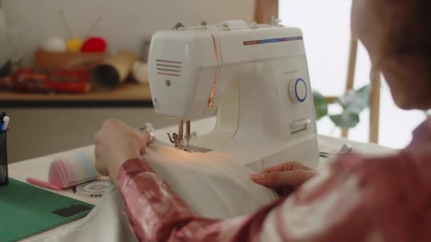 Sobre el hombro del sastre irreconocible que trabaja con la tela en la máquina de coser en el taller - Metraje, vídeo