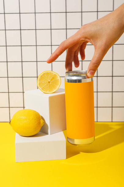 Cínová plechovka, citróny a ruka na žlutém stole na světlém pozadí - Fotografie, Obrázek
