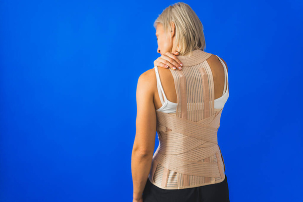 Junge Frau in Rückenlehne vor blauem Hintergrund, Frau mit Rückenproblemen. Hochwertiges Foto - Foto, Bild