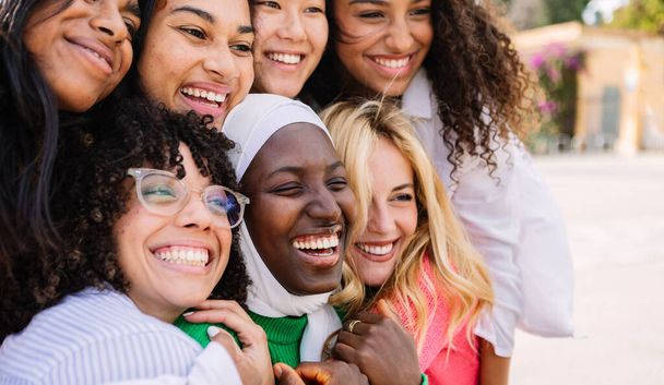 アウトドアで楽しむ女性の多様なグループ. 市街地で抱き合って笑う多民族の少女たち. 女性の友情コンセプト - 写真・画像