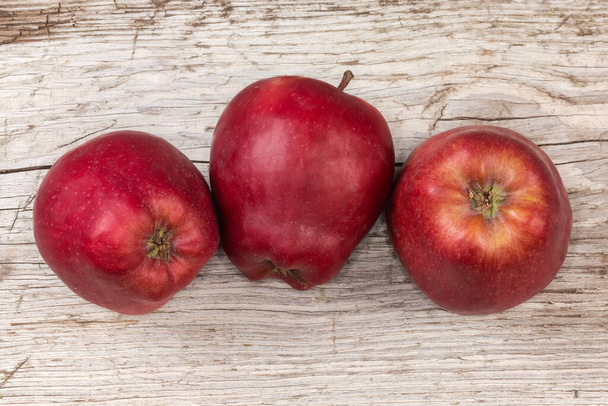 Несколько темно-красных яблок на старой потрескавшейся деревянной поверхности, вид сверху - Фото, изображение