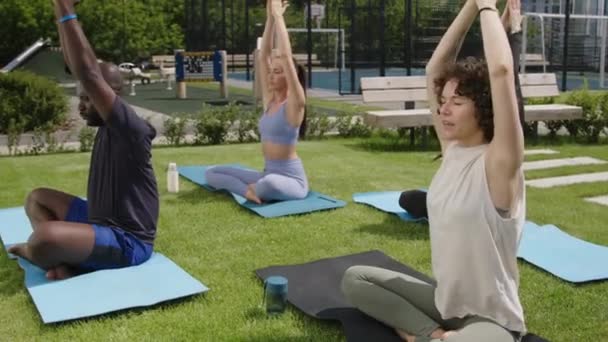 Lato filmato completo di yogi caucasico femminile che praticano yoga per diversi gruppi di studenti che ripetono asana e fanno segno namaste mentre sono seduti nel parco condominio - Filmati, video