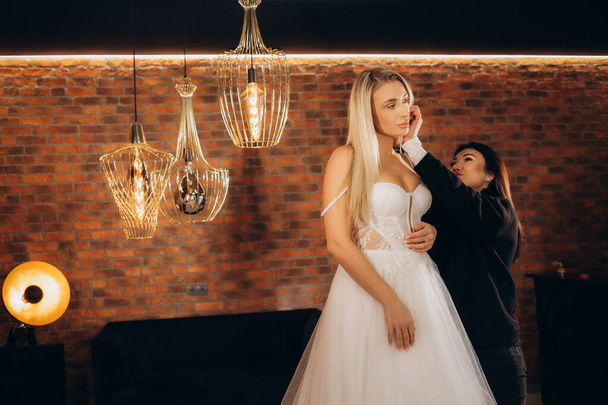 Berater im Hochzeitssalon hilft der Braut, ein Hochzeitskleid anzuziehen - Foto, Bild