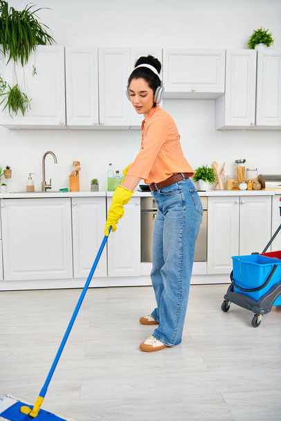 Uma mulher elegante em roupas casuais esfrega graciosamente o chão da cozinha com uma esfregona, exalando elegância e funcionalidade. - Foto, Imagem