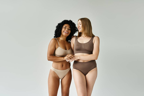 Two diverse women standing gracefully in cozy pastel underwear. - Photo, Image