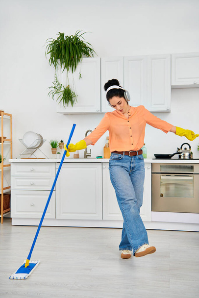 Egy elegáns nő alkalmi öltözékben kecsesen takarítja a padlót egy felmosóval az otthonában.. - Fotó, kép