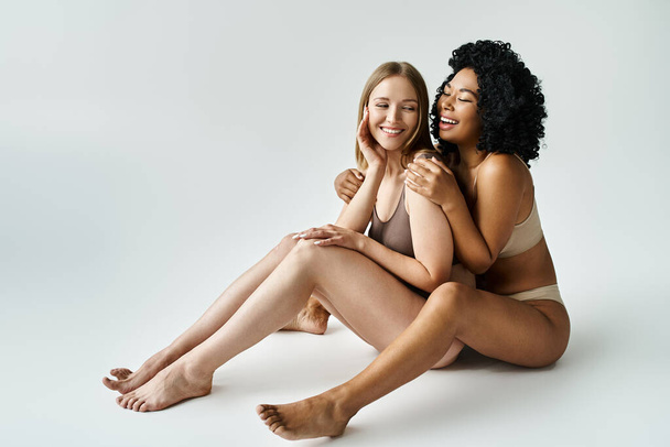 Twee diverse vrouwen in gezellig pastelondergoed tegen een witte achtergrond. - Foto, afbeelding