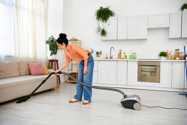 Eine stilvolle Frau in lässiger Kleidung saugt effizient ein Wohnzimmer, so dass es makellos und frisch ist. - Foto, Bild