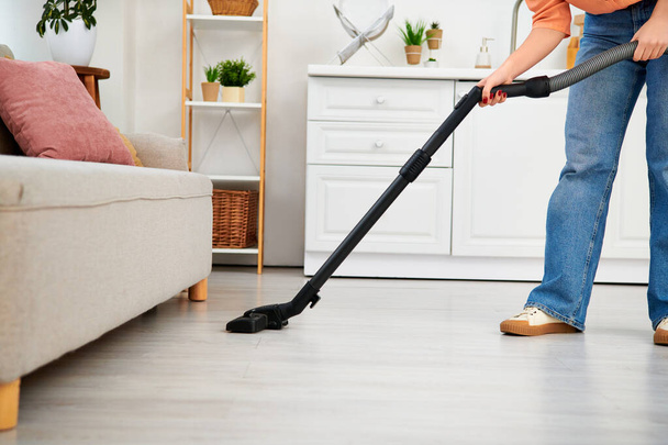 Uma mulher elegante em traje casual usando um aspirador de pó para arrumar o chão de sua casa. - Foto, Imagem