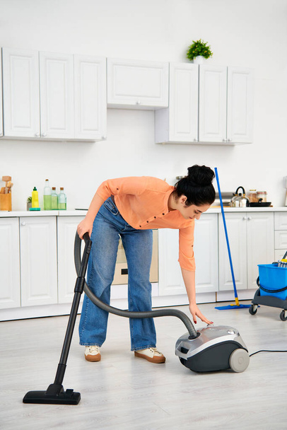 カジュアルな服装のスタイリッシュな女性は,掃除機を使用してキッチンフロアを情熱的にきれいにします. - 写真・画像