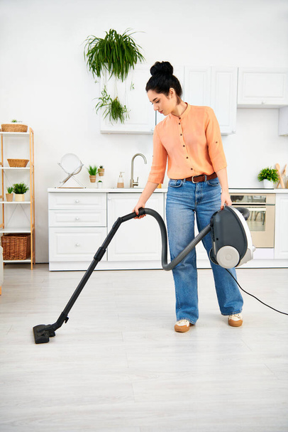 Стильна жінка в повсякденному вбранні ефективно вакуумує свою кухонну підлогу, щоб тримати її вдома без плям. - Фото, зображення