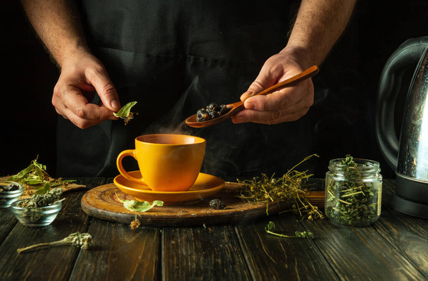 A man brews healthy tea from medicinal dry herbs. A hand holds a spoon with dry rose hips to add to a cup. Traditional medicine concept. - Photo, Image