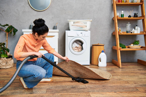 Una mujer elegante con atuendo casual limpia el suelo con una aspiradora en un entorno hogareño. - Foto, imagen