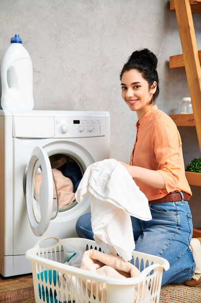 A stylish woman casually dressed, seated on the floor beside a washing machine. - Photo, Image