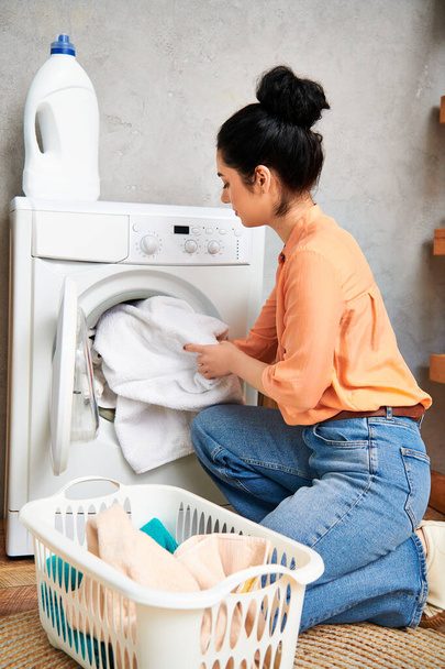 Μια κομψή γυναίκα με casual ενδυμασία κάθεται δίπλα σε ένα πλυντήριο ρούχων, επικεντρωμένη στον καθαρισμό του σπιτιού της. - Φωτογραφία, εικόνα