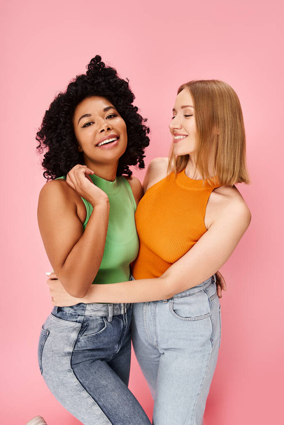 Dvě ženy, různorodé a stylové, se vřele objímají na měkkém růžovém pozadí. - Fotografie, Obrázek