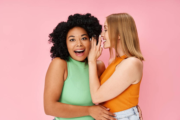 Two diverse women in casual attire pose gracefully against a soft pink backdrop. - Photo, Image