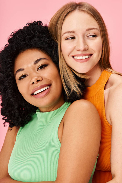 Two women in cozy attire hugging against a pink background. - Photo, Image