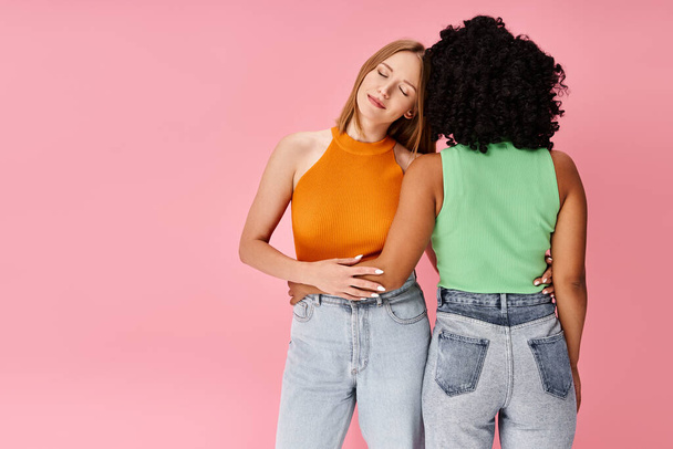 Two diverse women in cozy casual attire stand against a vibrant pink background. - Photo, Image