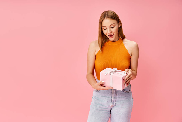 Женщина в удобной повседневной одежде держит розовую подарочную коробку в руках. - Фото, изображение