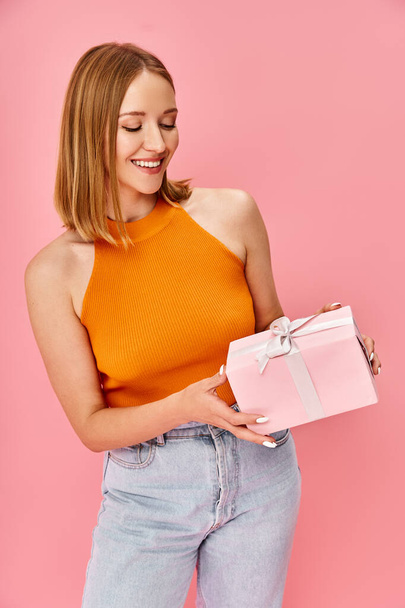 Uma mulher em um top laranja segura uma caixa de presente branca. - Foto, Imagem