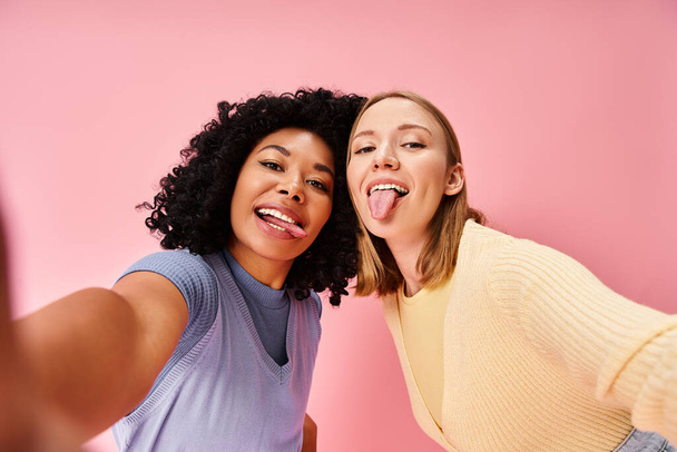 Dos mujeres en atuendo casual tomando una selfie frente a una pared rosa. - Foto, imagen