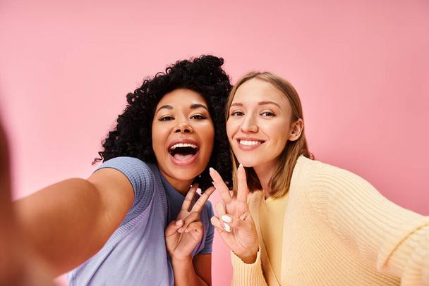 Kaksi naista rento puku poseeraa selfie edessä vaaleanpunainen seinä. - Valokuva, kuva