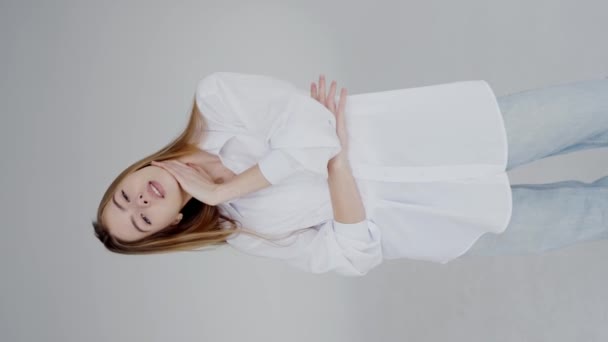 A woman in a white shirt and blue jeans is lying on her back, with a smile on her face. Her eyelashes are fluttering as she playfully raises her thumb in a happy gesture - Footage, Video