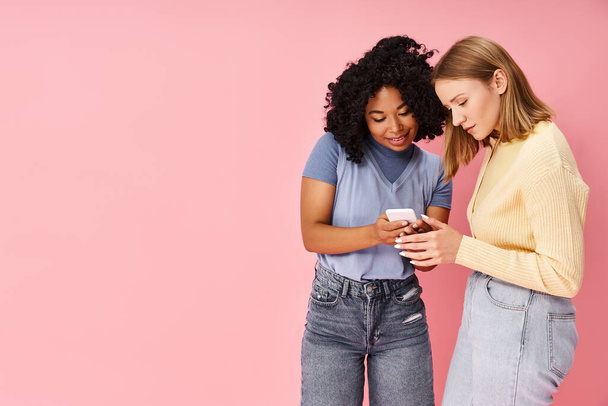 Zwei unterschiedliche Frauen in legerer Kleidung stehen zusammen, in ein Handy vertieft. - Foto, Bild