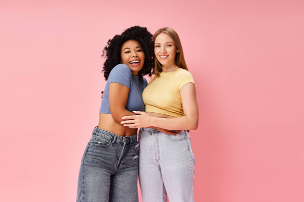 Two diverse women in cozy casual attire stand side by side on a pink background. - Photo, Image