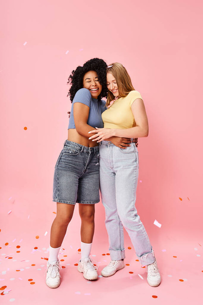 Dos mujeres atractivas y diversas se abrazan calurosamente frente a un telón de fondo rosa suave. - Foto, imagen